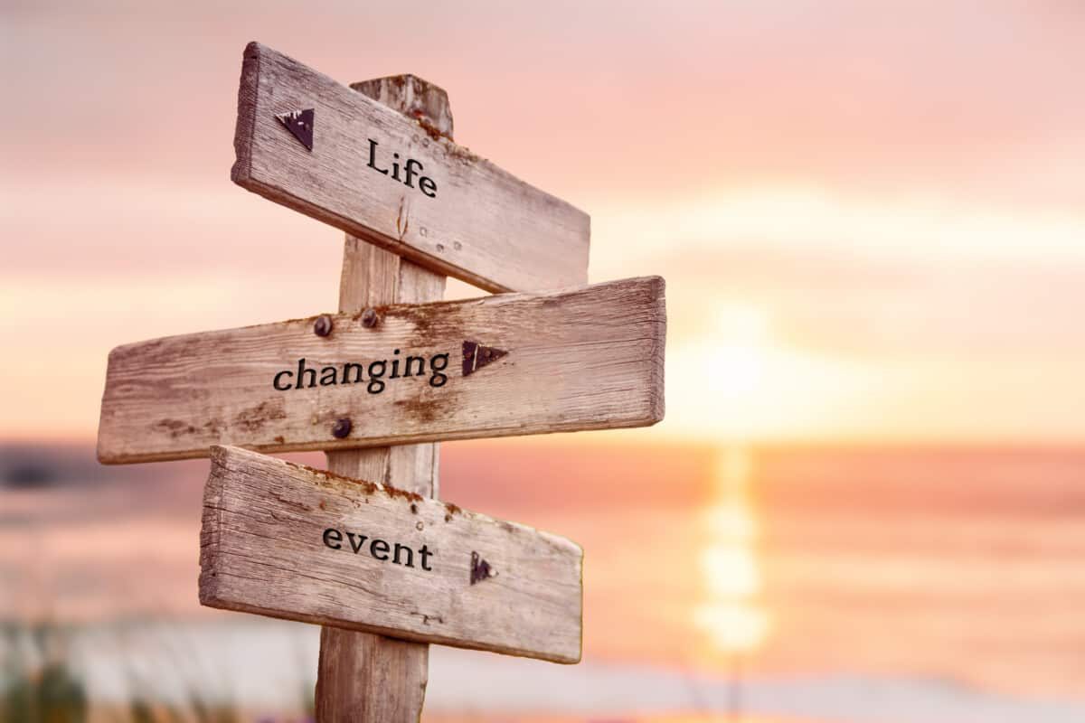 life changing event text quote on wooden crossroad signpost outdoors on beach with pink pastel sunset colors. Romantic theme.